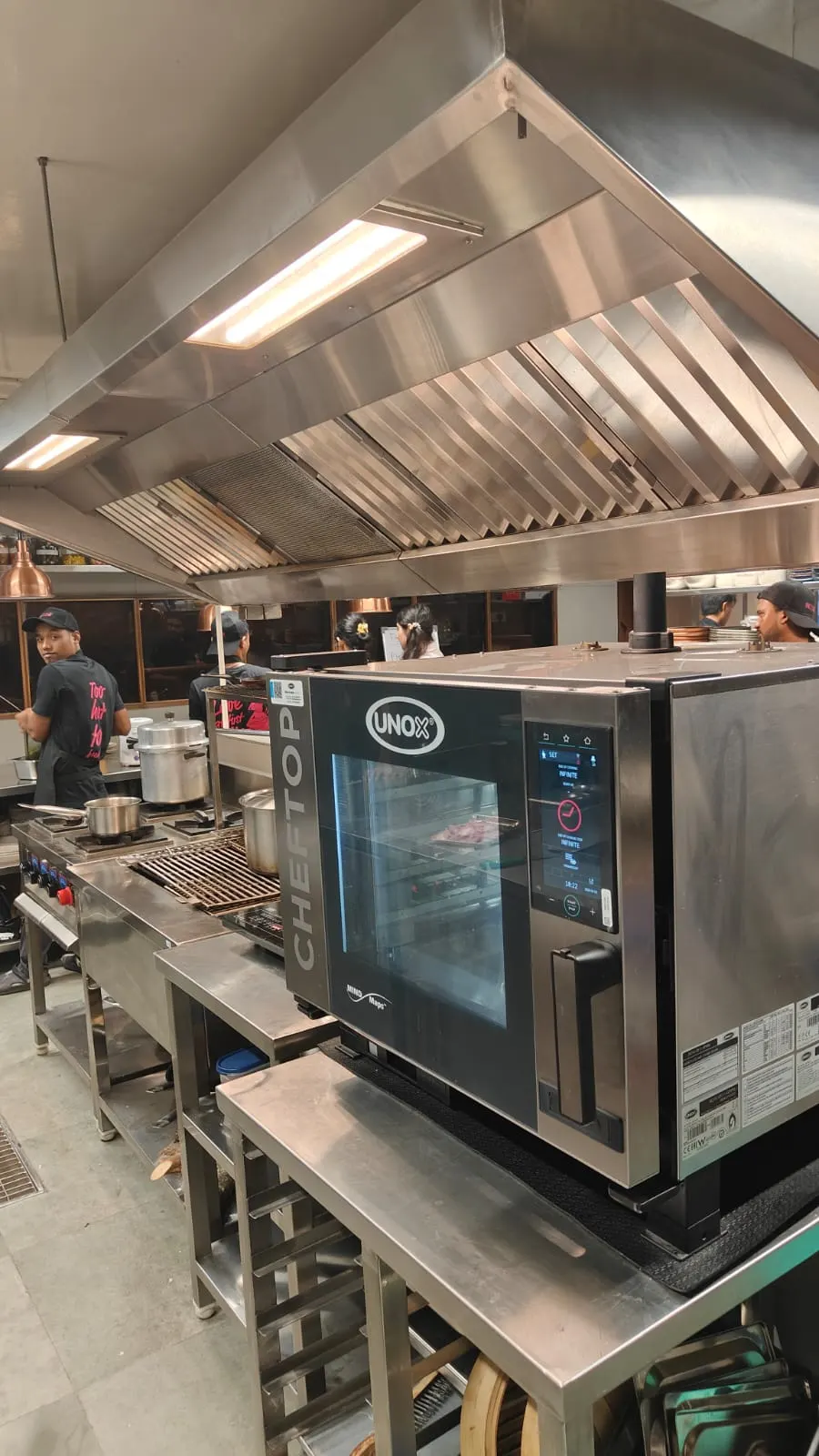 Combi oven installed on a stainless steel stand under an exhaust hood