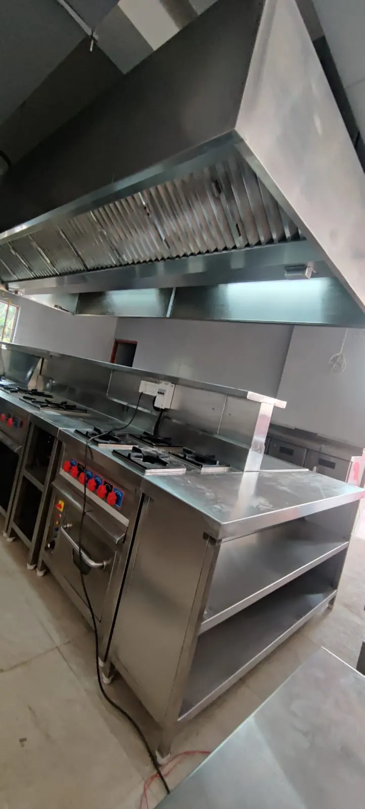 Cooking range with overhead pass shelf under a stainless steel wall hood