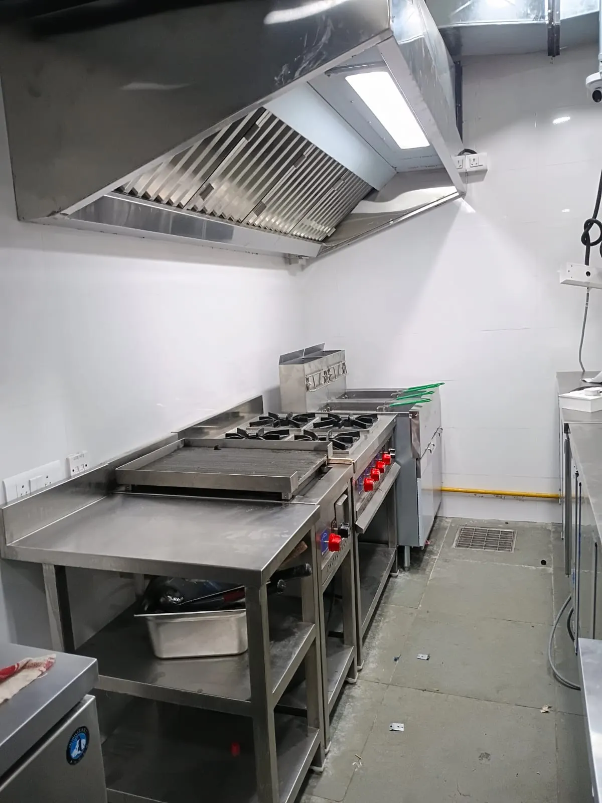 Stainless steel four burner cooking range with hot plate under a wall exhaust hood
