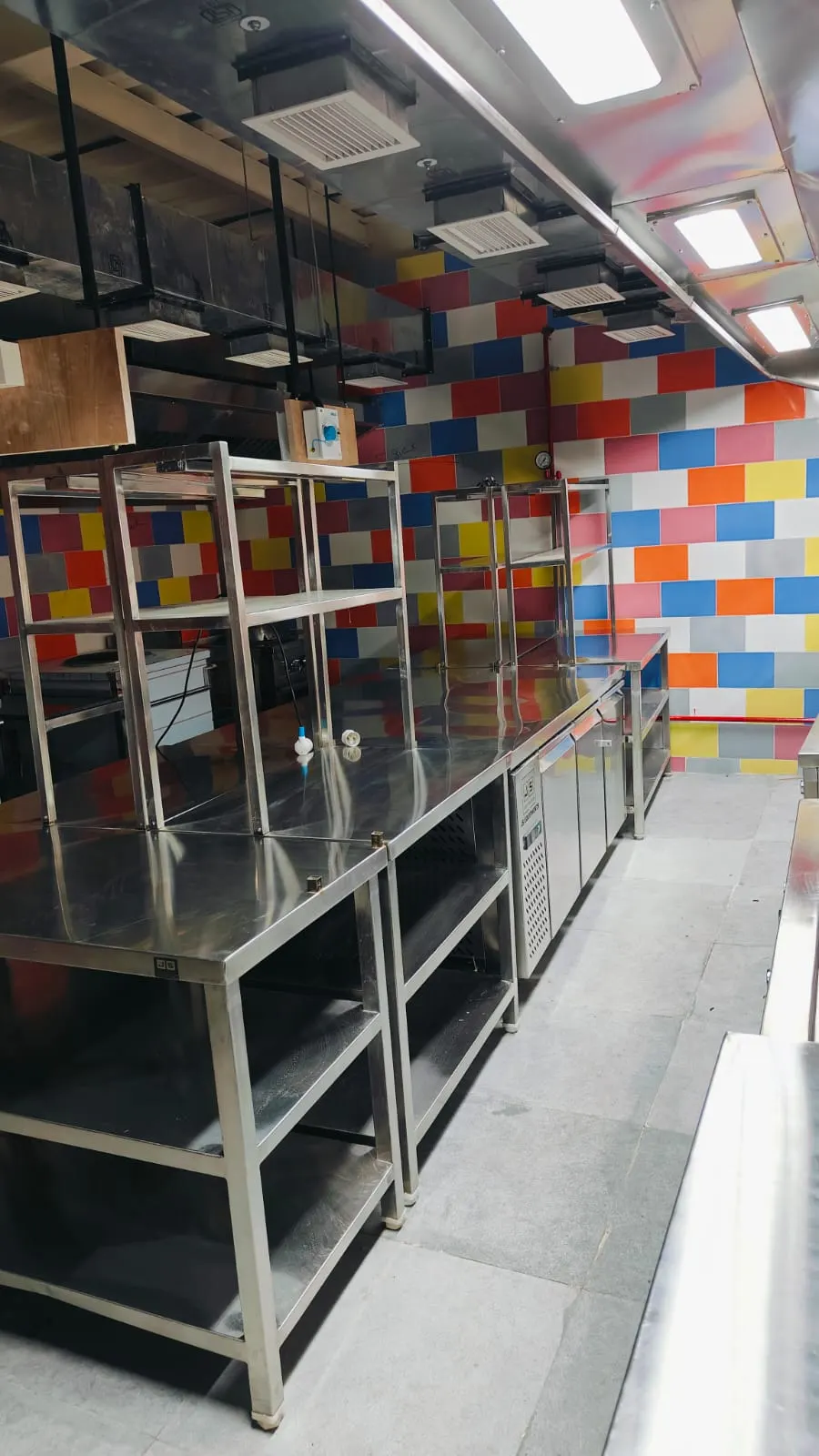 Stainless steel work tables with overhead racks in a tiled kitchen